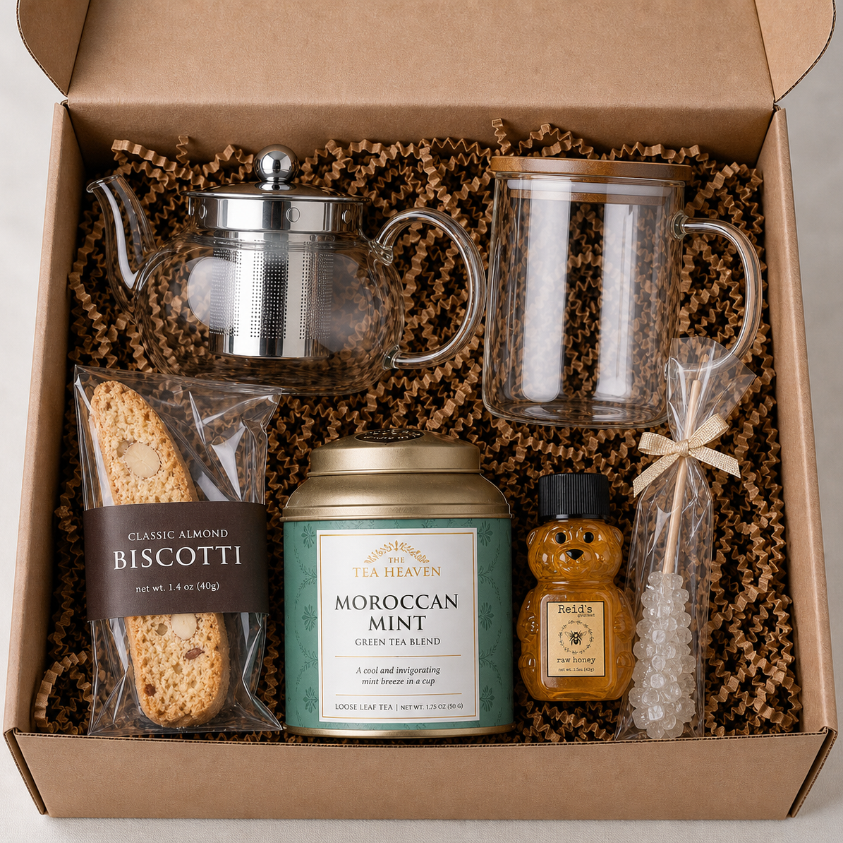 Gift box with glass tea pot, tea mug, loose leaf tea, biscotti, and honey and a sugar stick.